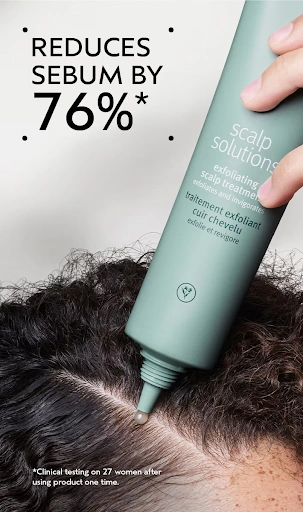 A hand applies Aveda Scalp Solutions exfoliating scalp treatment to a person's scalp, with text stating it reduces sebum by 76% after one use based on clinical testing on 27 women. | Anaala Salon and Spa, Madison WI