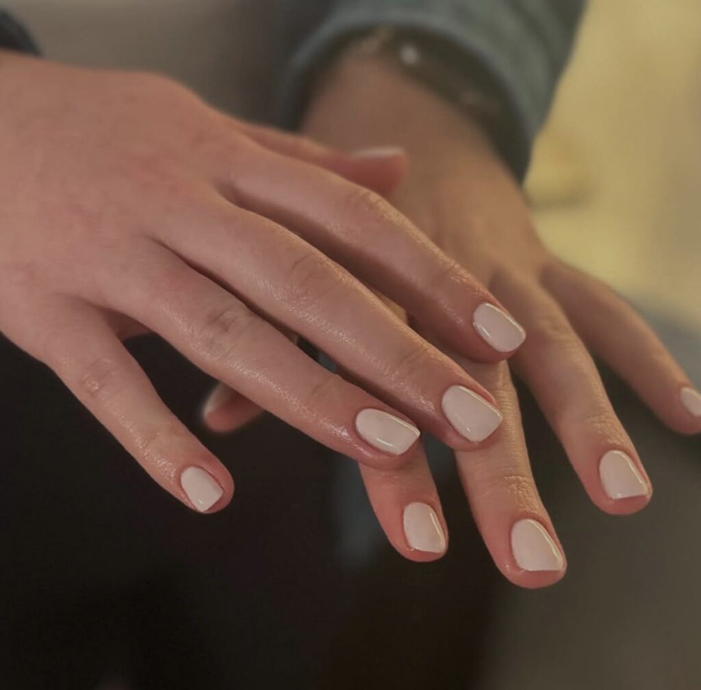 A person’s hands with neatly manicured nails painted in a pale pink color, shown against a blurred background at a spa known for the best facial in Madison WI. | Anaala Salon and Spa, Madison WI