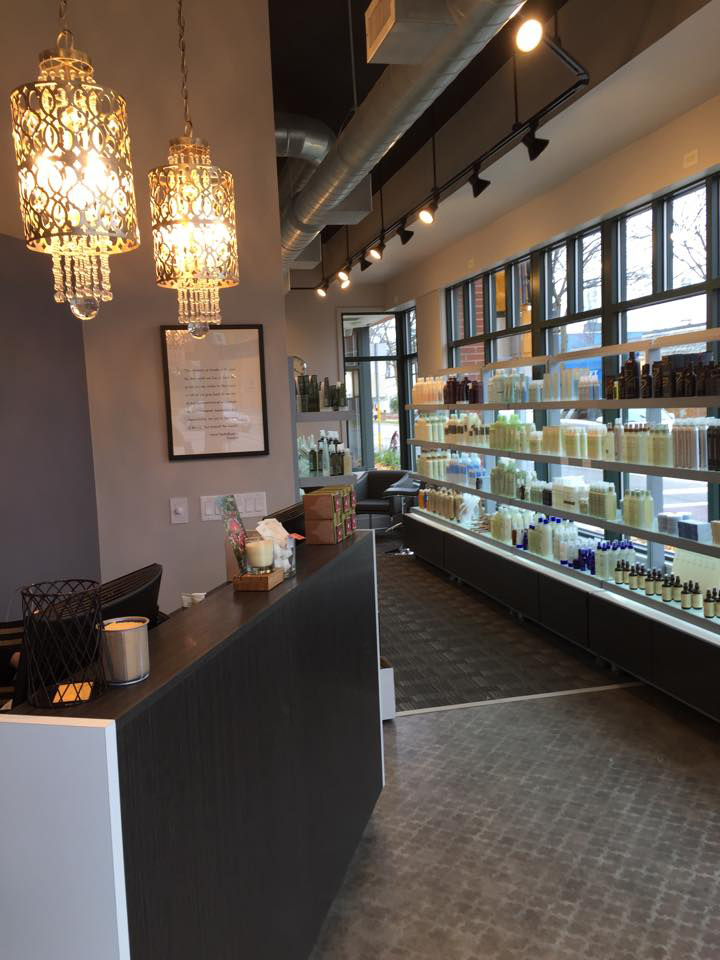 Modern salon interior with hanging chandeliers, a reception desk, and shelves lined with hair and beauty products near large windows—experience the best salon in Madison WI for premium smoothing straightening services. | Anaala Salon and Spa, Madison WI