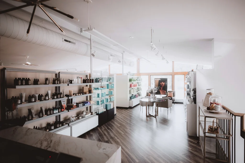 Bright, modern salon interior with wooden floors, shelves displaying hair and beauty products, a reception counter, and a seating area near large windows—experience the best salon in Madison WI for expert care and style. | Anaala Salon and Spa, Madison WI